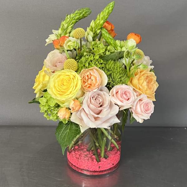 Mixed roses and green blooms arranged in a clear glass vase with pink stones.
