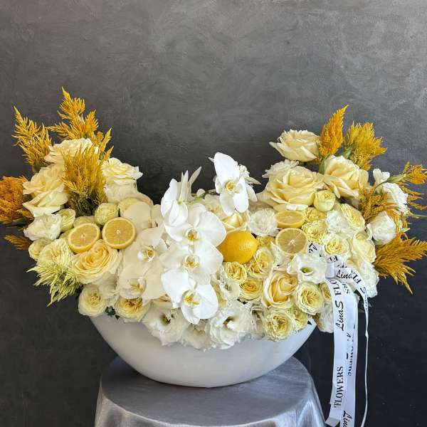Cream and white floral arrangement with orchids and roses in a white bowl