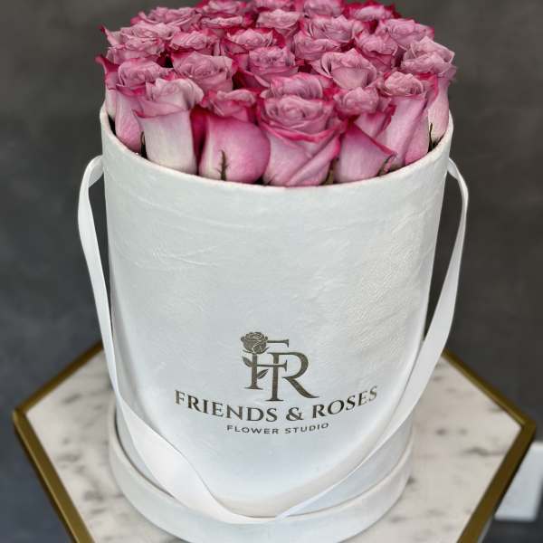 Pink roses arranged in a white round hat box with ribbon handles