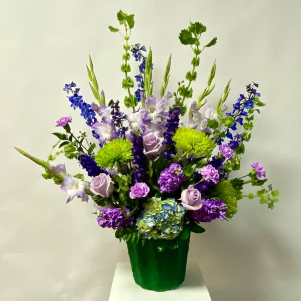 Tall mixed bouquet of purple, blue, and green flowers in a green container