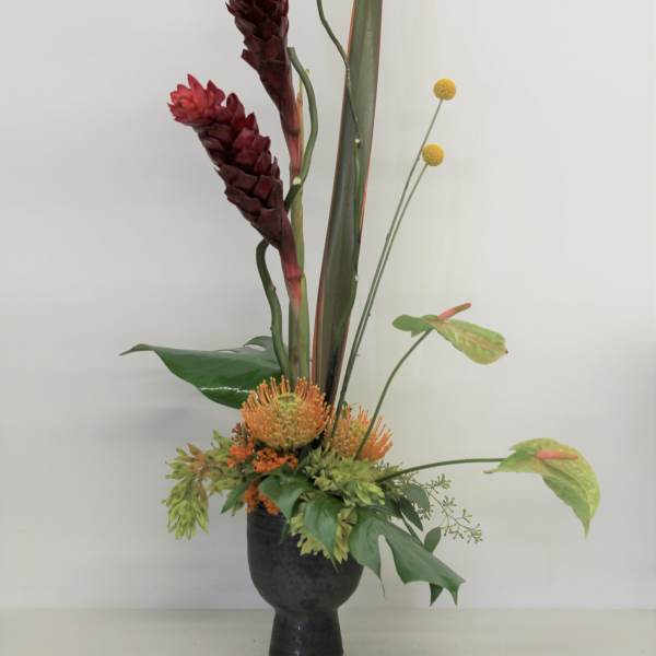 Tall tropical arrangement in a black vase with red blooms and orange accents