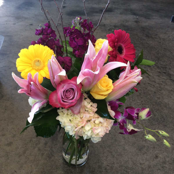 Mixed bouquet in a clear glass vase with pink lilies, roses, gerbera daisies, and purple blooms