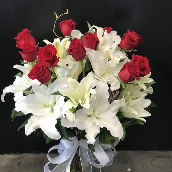 Bouquet of red roses and white lilies in a glass vase with a white ribbon