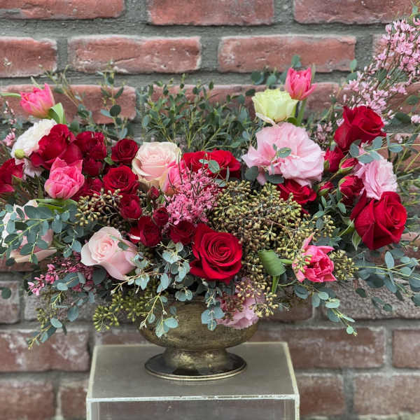 Low floral arrangement of red and pink roses in a gold vase