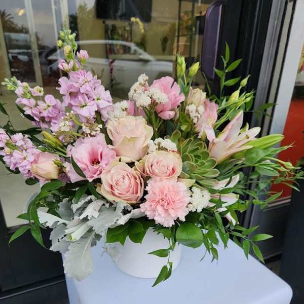 Low arrangement of soft pink roses, carnations, lilies and succulents in a white vase