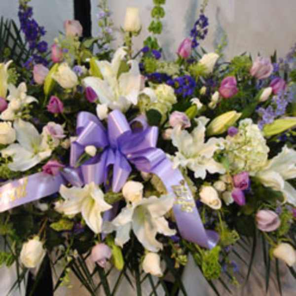 Large floral spray with white lilies, purple flowers, and a lavender ribbon