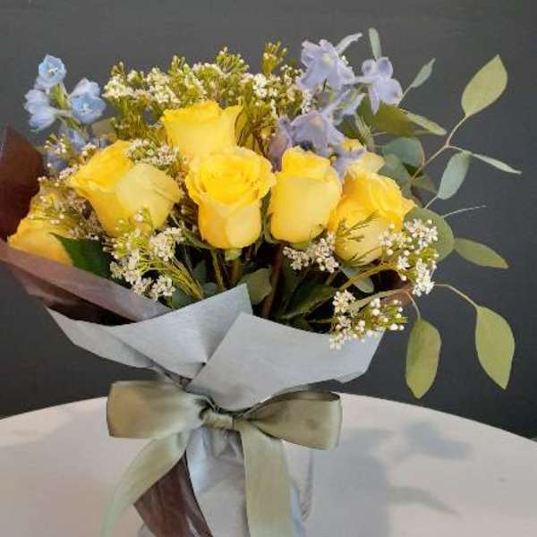 Yellow roses with small blue flowers in a wrapped bouquet