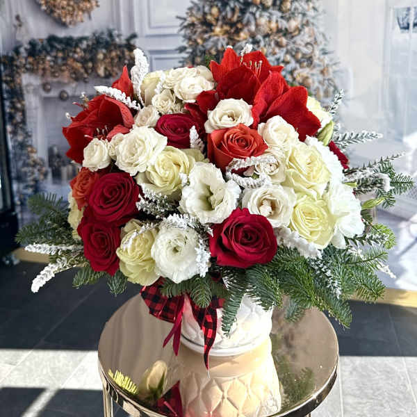 Bouquet of red and white roses in a white vase with evergreen accents