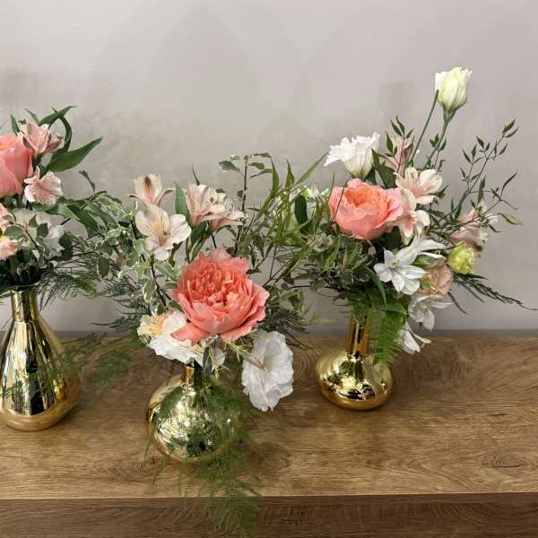 Three floral arrangements in gold vases with pink and white blooms