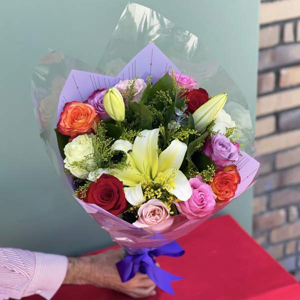 Bouquet of multicolored roses and white lilies wrapped in purple paper