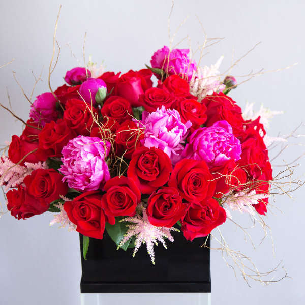 Low arrangement of red roses and bright pink peonies in a black rectangular vase
