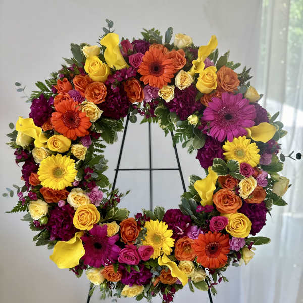 Large circular floral wreath on a stand with yellow, orange, pink, and purple blooms