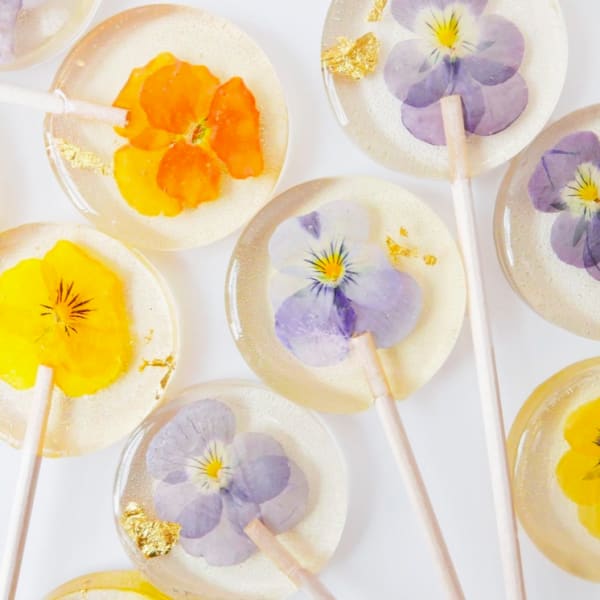 Clear lollipops with pressed yellow and lavender flowers and gold leaf on a white background