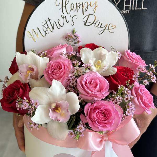 Pink and red roses with white orchids in a round box for Mother’s Day