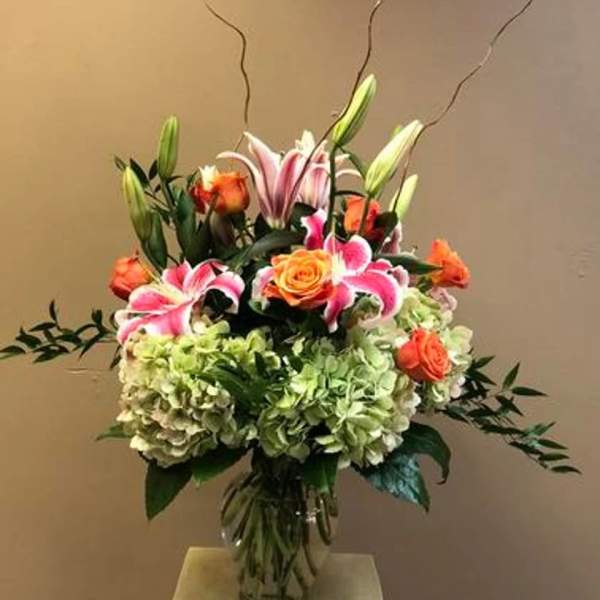 Bouquet of pink lilies, orange roses, and green hydrangeas in a glass vase