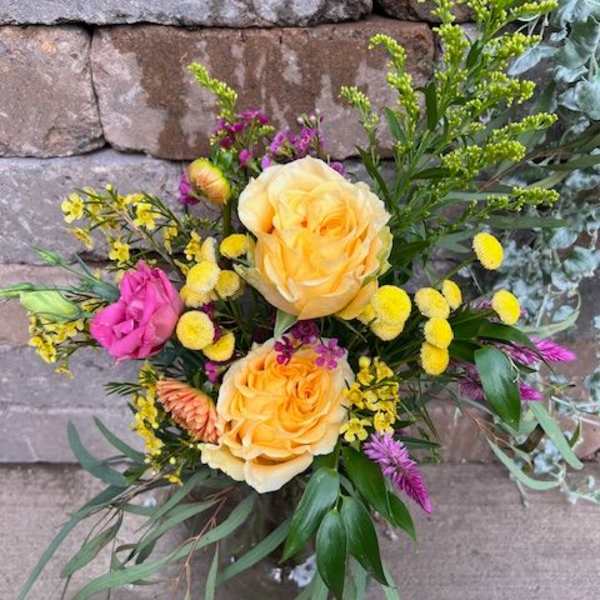 Mixed bouquet of yellow and pink blooms in a clear glass vase against a stone wall