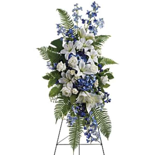 Standing floral spray with white lilies, roses, and blue flowers on an easel