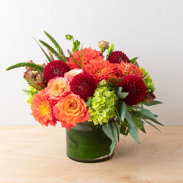 Orange and red mixed flower arrangement in a green glass vase