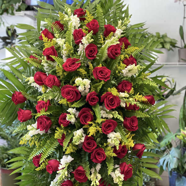 Tall standing spray of red roses with white flowers and yellow accents on lush greenery.