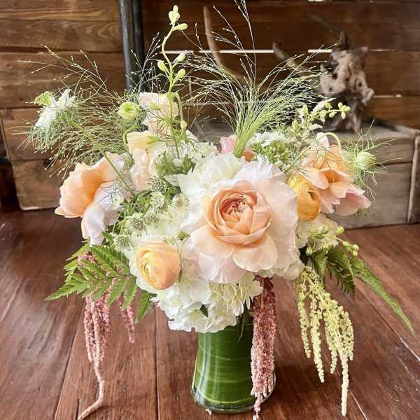 Peach roses and white blooms in a green glass vase