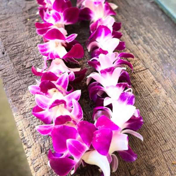 Two purple and white orchid leis laid on a wooden surface.