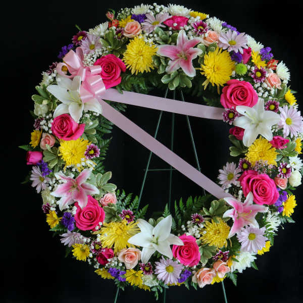 Circular floral wreath with pink ribbon and mixed blooms on a stand