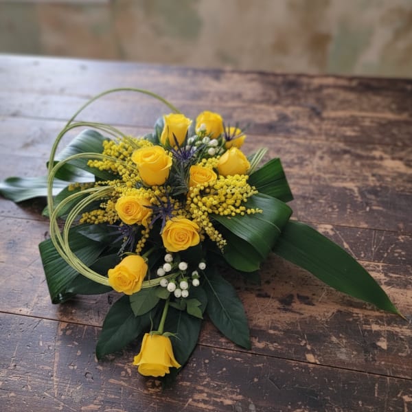 Low arrangement of yellow roses with white berries and looped grass on a wooden table