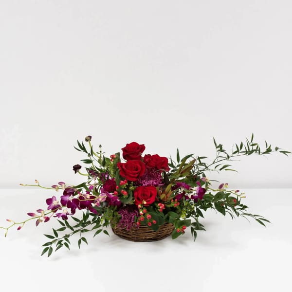 Basket arrangement of red roses and purple orchids