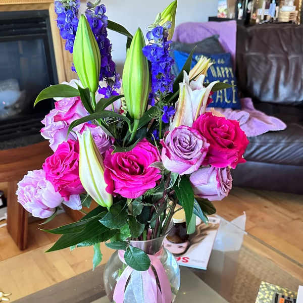 Bouquet of pink roses, purple lilies, and blue delphinium in a glass vase