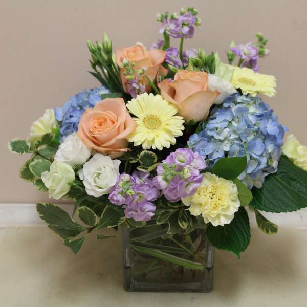Mixed bouquet of roses, hydrangeas, and daisies in a square glass vase