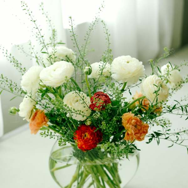 White and orange flowers arranged in a round glass vase