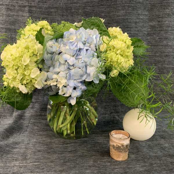 Hydrangea arrangement in a glass vase with a candle and white orb