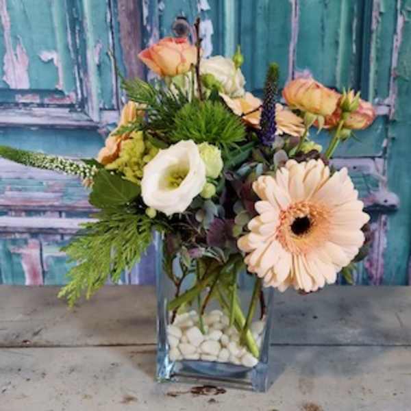 Peach and white flowers arranged in a clear square vase