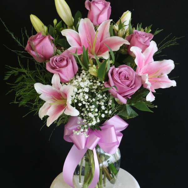 Pink roses and lilies in a glass vase with a pink ribbon