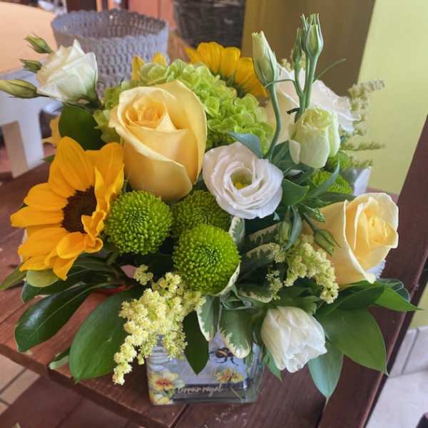 Bouquet of yellow roses, sunflowers, and white blooms in a glass vase