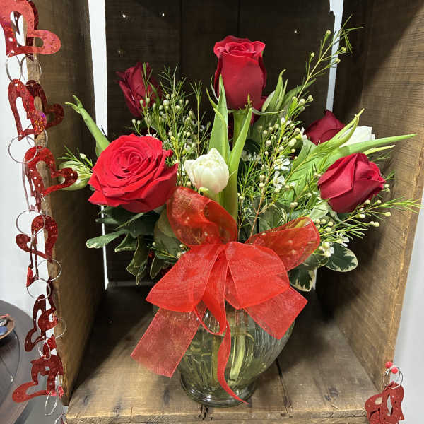 Red roses and a white tulip in a glass vase with a red bow