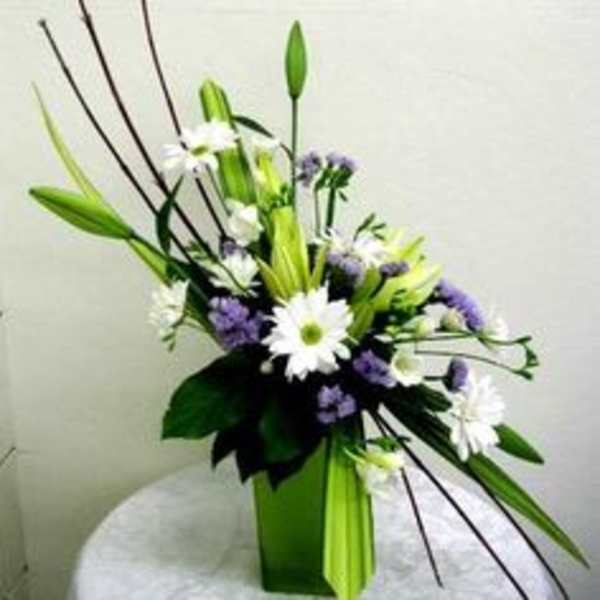Tall floral arrangement with white daisies and purple blooms in a green vase