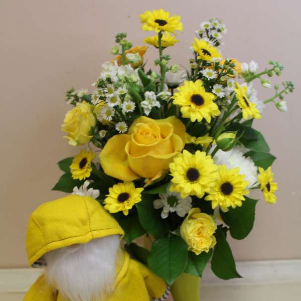 Yellow rose and daisy bouquet in a vase beside a small gnome figurine.