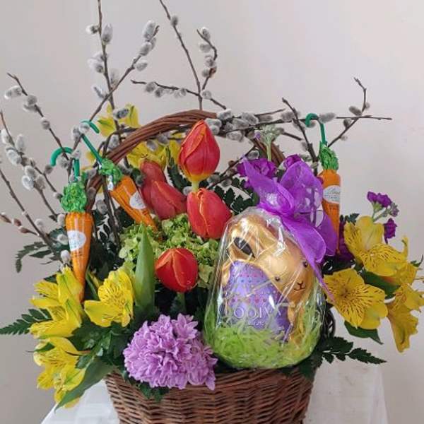 Wicker basket with tulips, yellow alstroemeria, purple blooms and a wrapped chocolate bunny.