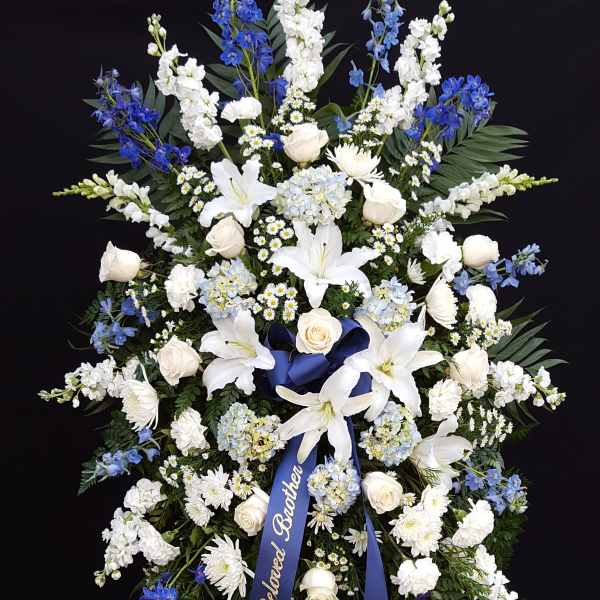 Large blue and white funeral spray with ribbon on an easel