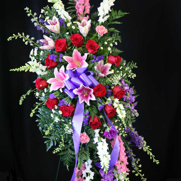 Standing floral spray with red roses, pink lilies, and purple ribbon