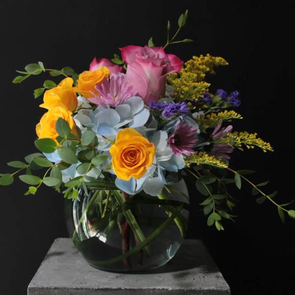Mixed bouquet of roses, hydrangea, and purple flowers in a glass vase