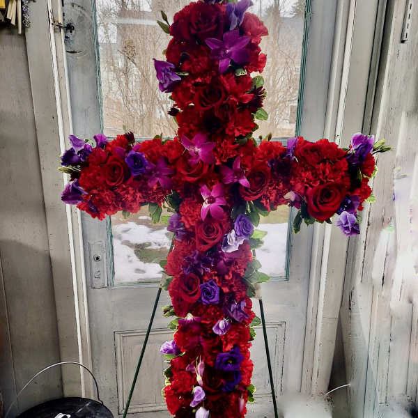 Cross-shaped floral arrangement of red and purple flowers on a stand