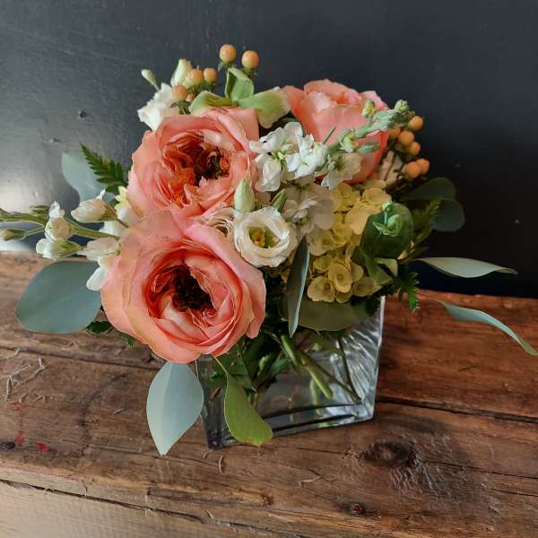 Peach roses and white flowers arranged in a square glass vase