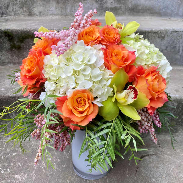 Orange roses and white hydrangeas arranged in a gray vase