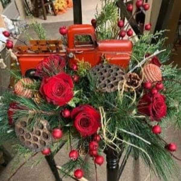 Red roses and holiday greenery arranged with a small orange toy truck