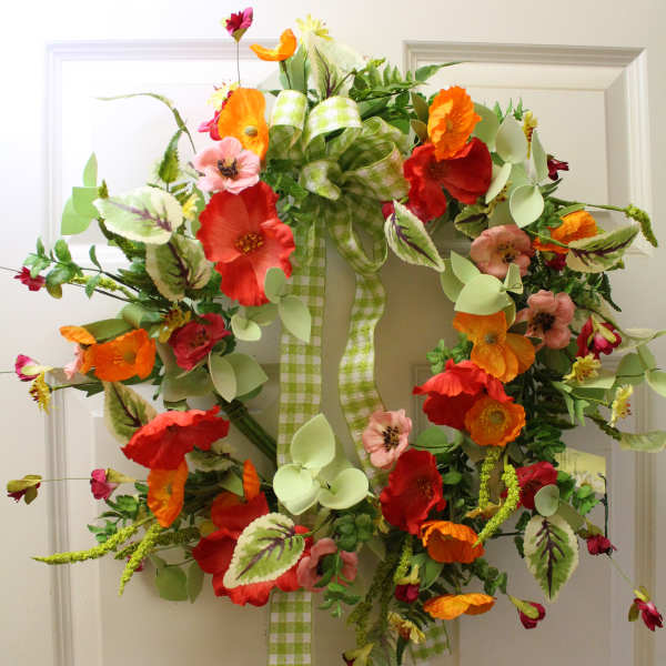 Colorful floral wreath with orange and red blooms on a white door