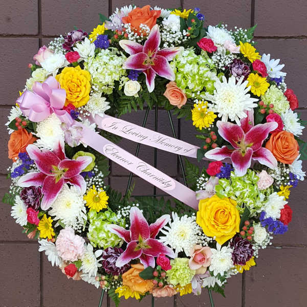 Heart-shaped floral wreath with pink lilies and mixed blooms on a stand