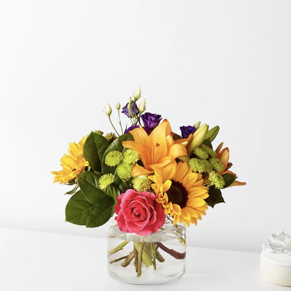 Mixed bouquet with roses, lilies, and sunflowers in a clear glass vase