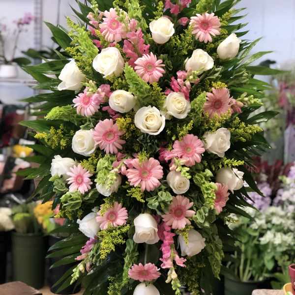 Tall standing spray with white roses and pink gerbera daisies on a green foliage backdrop.